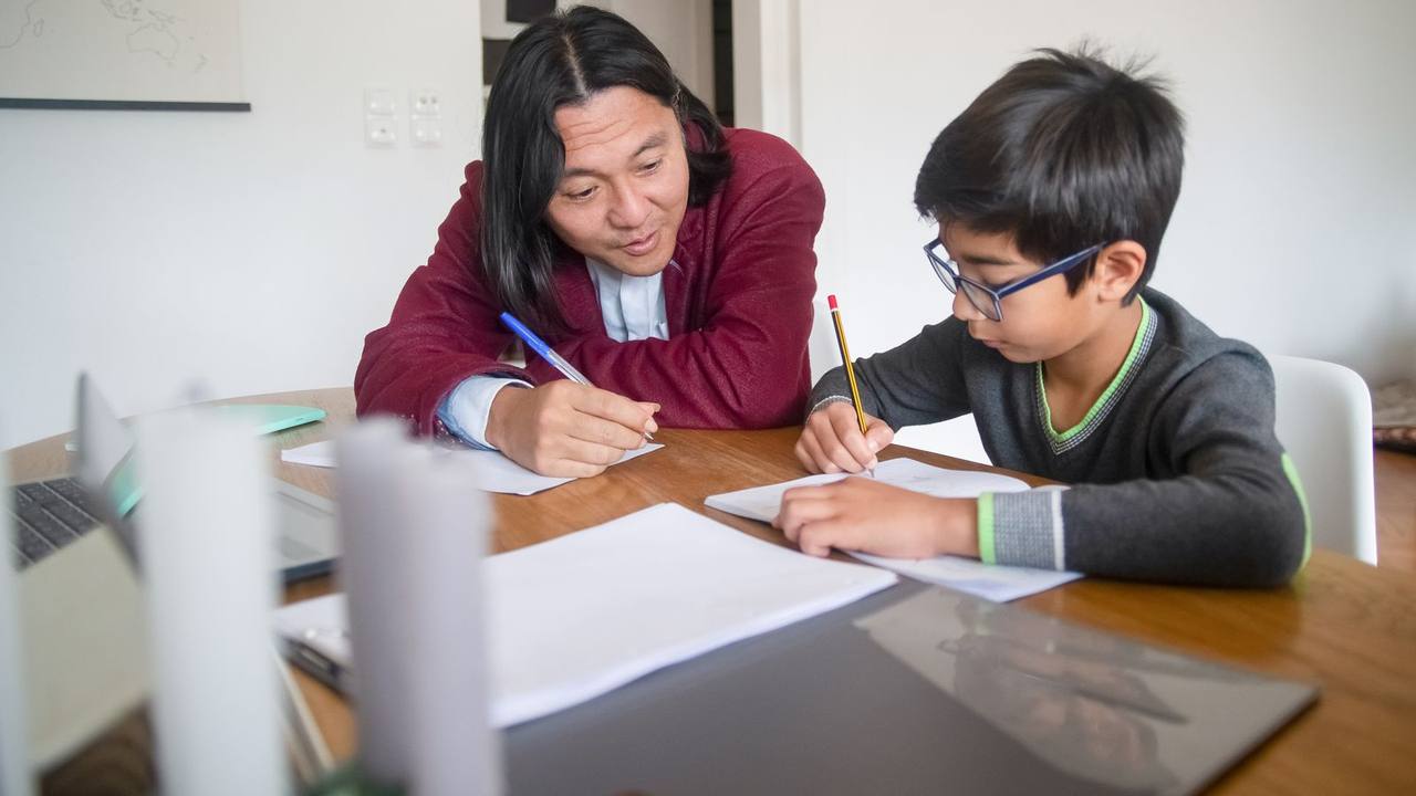 A tutor working through a worksheet with a school student at his dining table